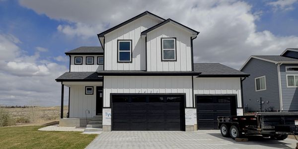 Modern two-story house with black garage doors under a cloudy sky.