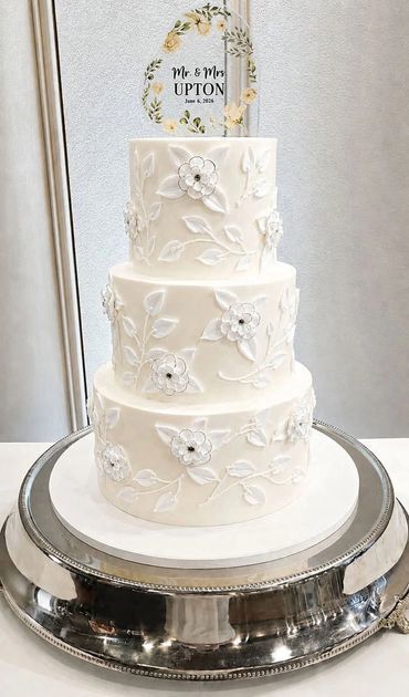 Elegant three-tier white wedding cake with floral decorations and a personalized topper.