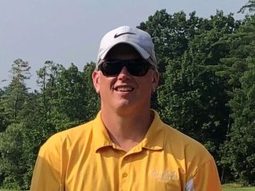 Man in yellow polo shirt wearing sunglasses and white cap outdoors.