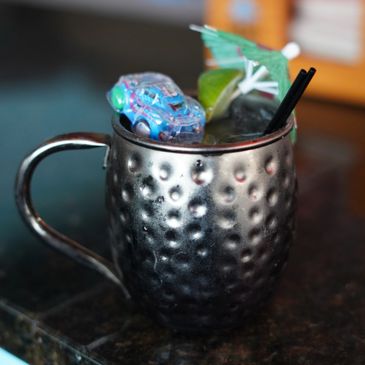 A hammered metal cup with a cocktail, toy car, umbrella, and straws.