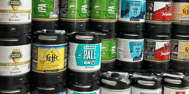 Stacked mini kegs of various craft beers from brands like Stella Artois, Leffe, Camden, Brewdog, and Jupiler.