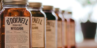 Row of O'Donnell Moonshine jars with varying colors on a wooden surface.