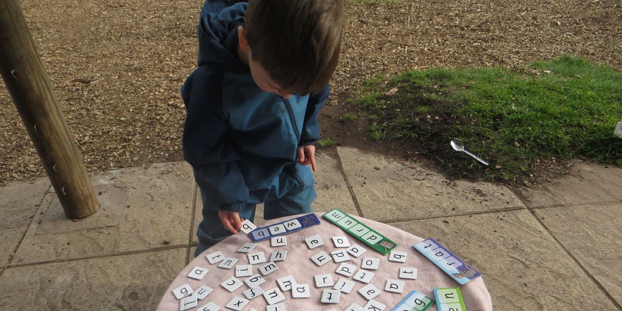 A child plays with letter tiles on a round table outdoors.