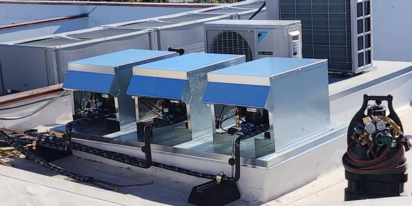 Three rooftop HVAC units with exposed components and connected piping.