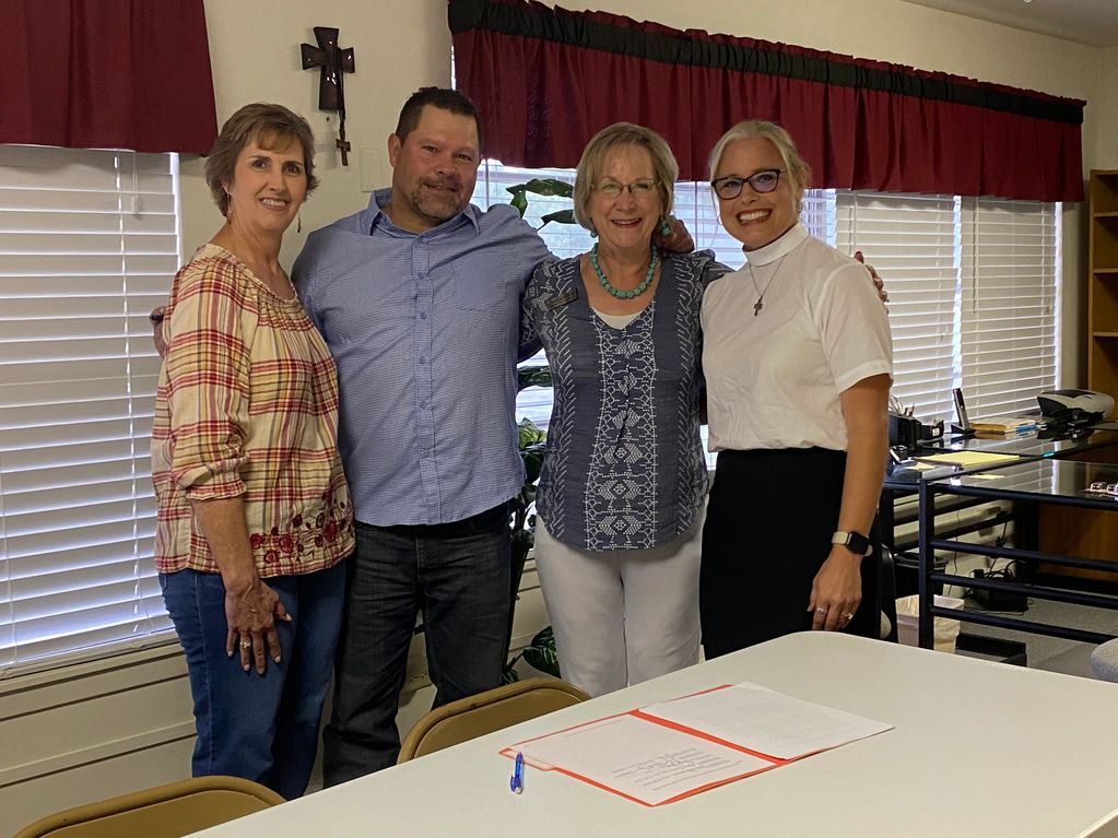 Four people standing together and smiling in a room with a table and documents.