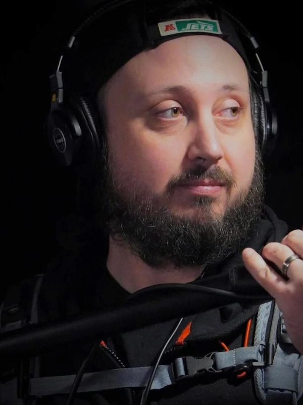 Bearded man wearing headphones and cap looking to the side.