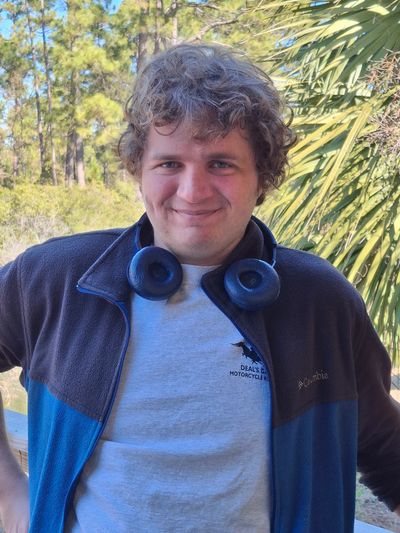 Smiling young man with curly hair and headphones outdoors.