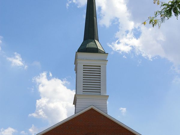 Tall church steeple against a bright blue sky with scattered clouds.
