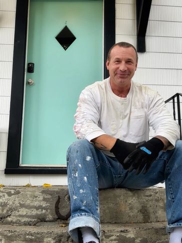Man in work clothes sits on steps in front of a turquoise door.
