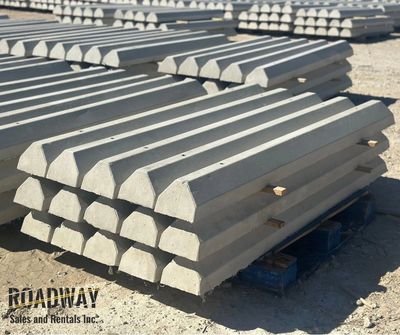 Stacks of concrete wheel stops made from precast concrete solutions neatly arranged on pallets at a construction site.