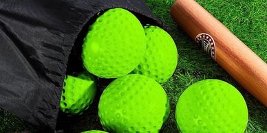 Bright green golf balls spilling from a black bag next to a wooden golf club on grass.