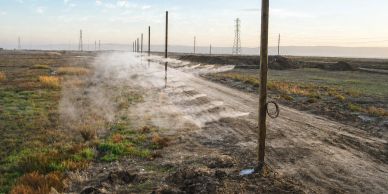 Irrigation system watering a barren field with misty spray at sunset.
