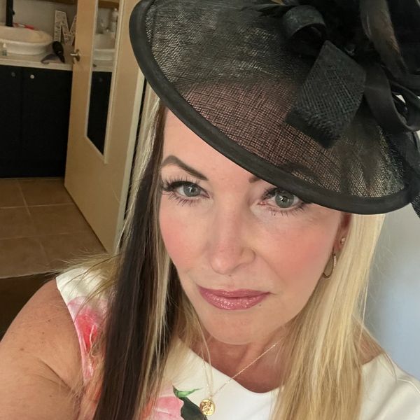 Woman with two-toned hair wearing a floral dress and a black fascinator hat.