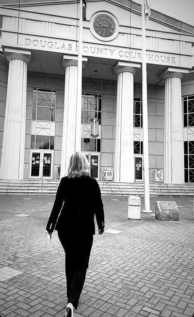 Woman walks towards the Douglas County Courthouse, a building with prominent columns and a clock.