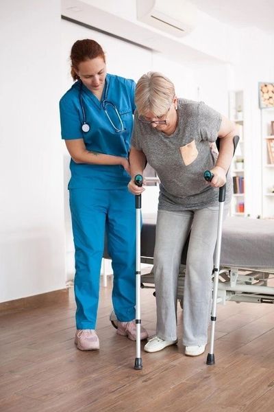 Nurse assisting elderly woman with crutches to stand.