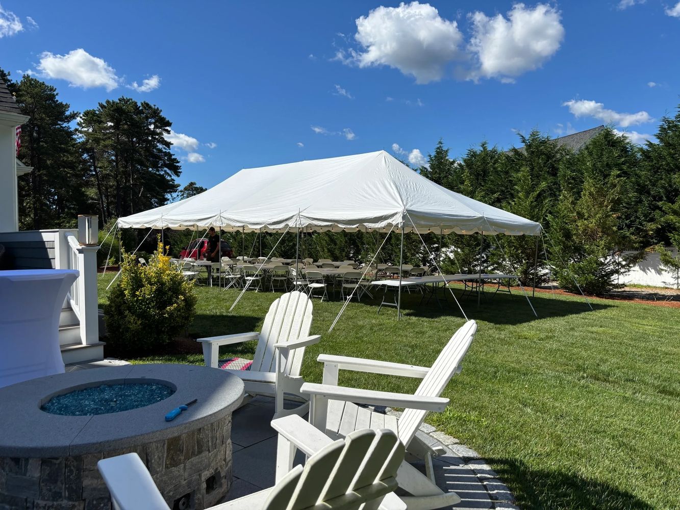 White outdoor tent set up with chairs and tables under a clear blue sky.