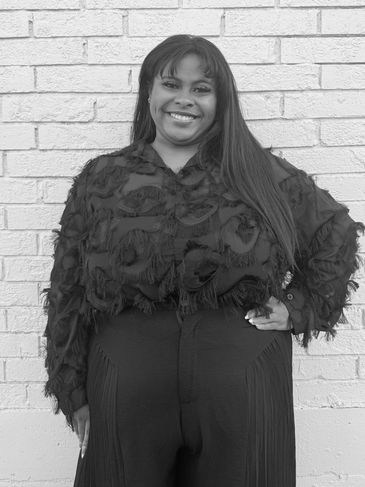 Smiling woman posing confidently against a brick wall in textured black clothing.