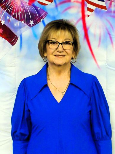 Woman smiling in a blue dress with patriotic decorations in the background.