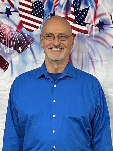 Smiling man in blue shirt with patriotic American decorations in the background.