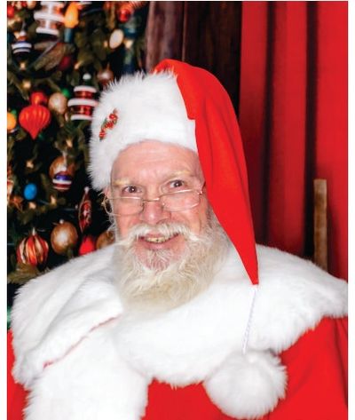 Smiling Santa Claus in red suit and hat by a decorated Christmas tree.