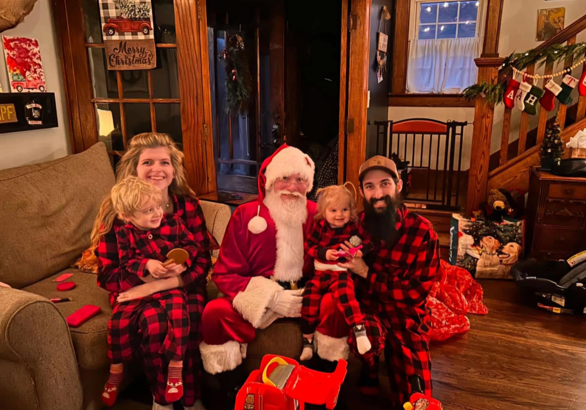 Family in matching red plaid pajamas with Santa Claus during Christmas.