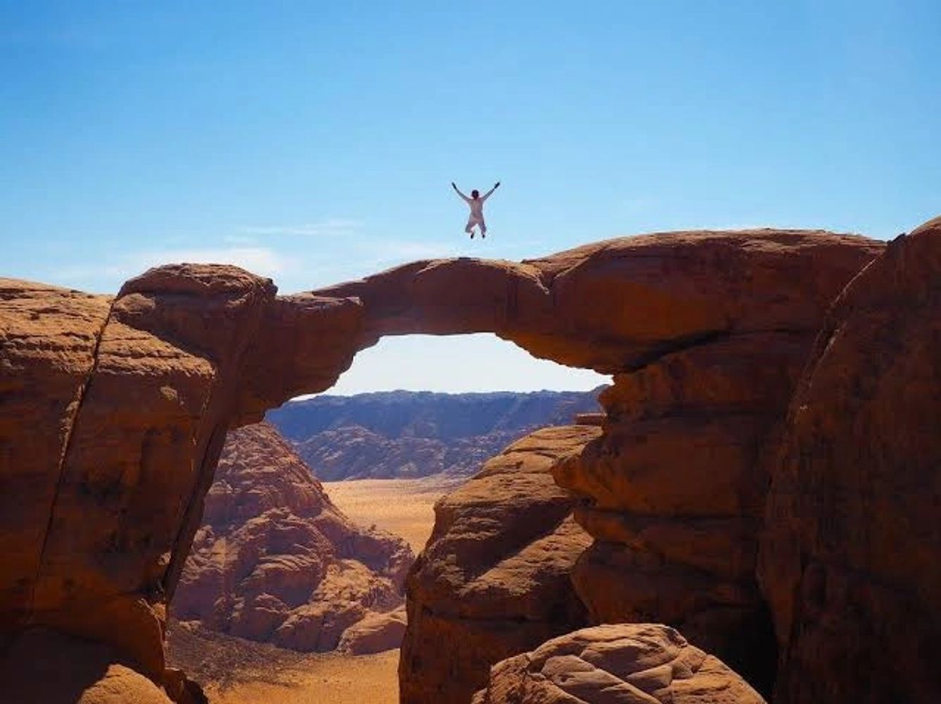 Person jumping on a natural rock arch in a desert.
