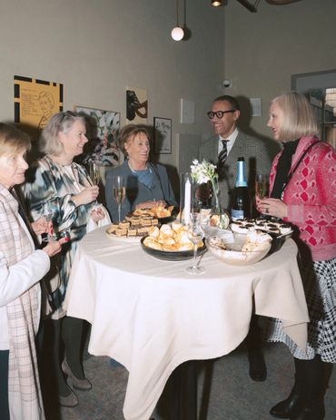 Five people enjoying drinks and desserts around a table at a social gathering.