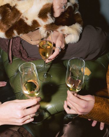 Three people holding champagne glasses on a green leather couch.