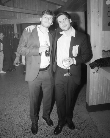 Two men in suits posing with drinks at an indoor event.