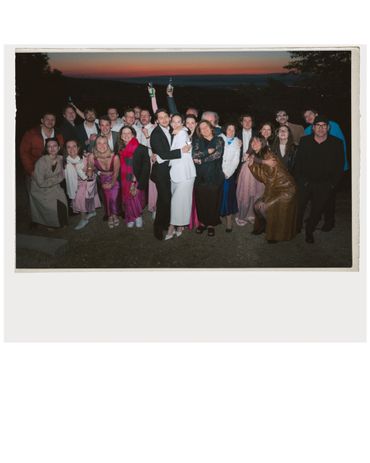 Group of people posing happily outdoors during sunset, some holding drinks.