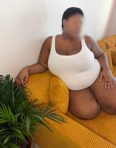 Person in white swimsuit sitting on a mustard yellow couch next to a green plant.