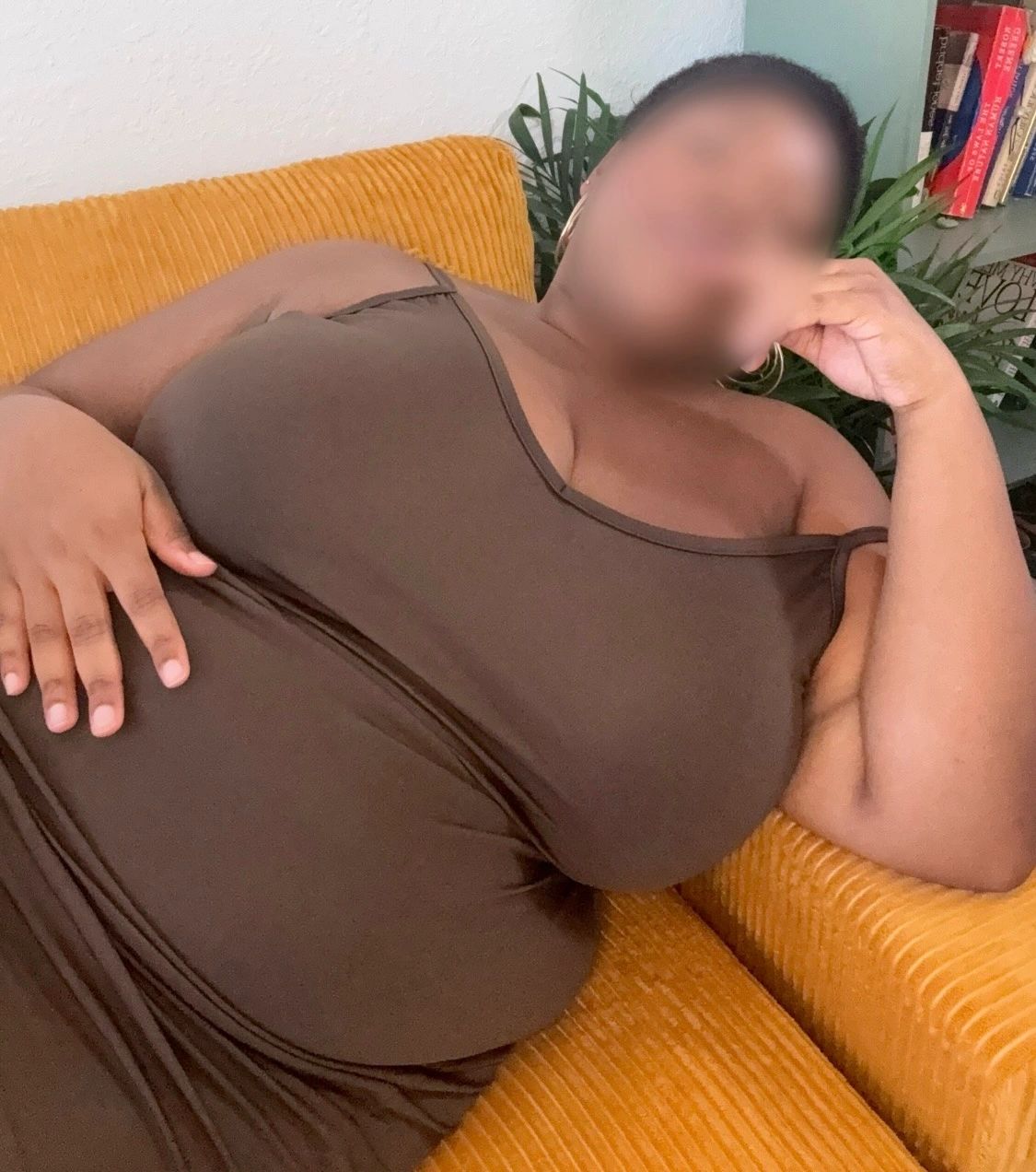 A person reclining on a mustard-yellow couch wearing a brown dress.