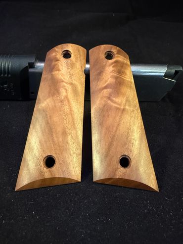 Two wooden grips for a handgun displayed on a black surface.
