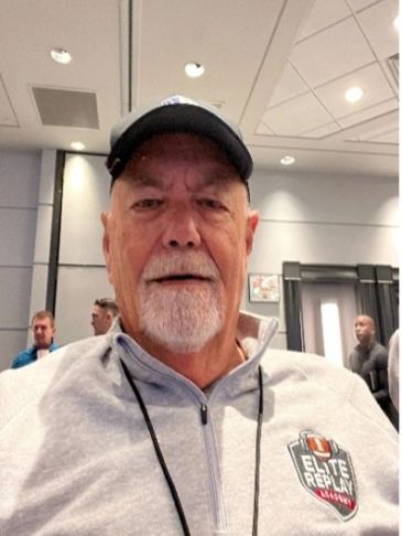 Older man wearing a cap and Elite Replay sweatshirt indoors.