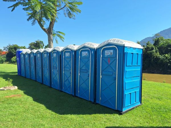 A line of blue portable toilets on green grass under a clear sky.