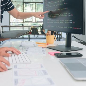 Person pointing at code on a computer monitor.