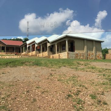 A row of simple buildings with metal roofs on a grassy hill under a blue sky.