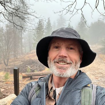 Man in outdoor gear smiling on a foggy hiking trail.