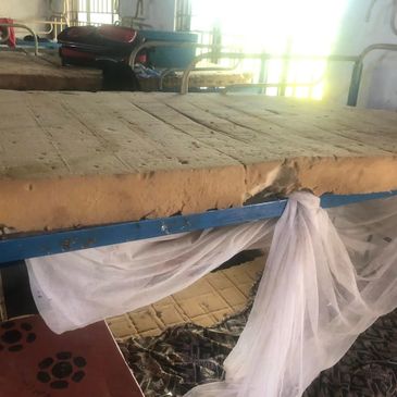 Worn-out bunk beds with old mattresses and a tied mosquito net in a dim room.