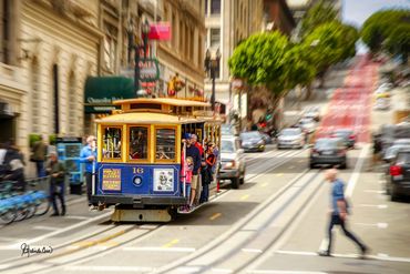 A blur of a San Franciso street culminates in a cable car which is in sharp focus. Cars and people a