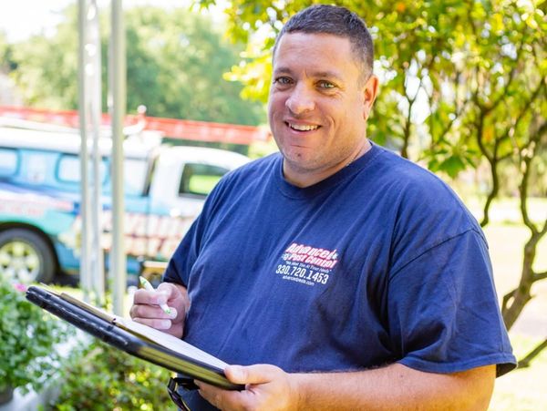 Smiling pest control worker holding a clipboard outdoors.