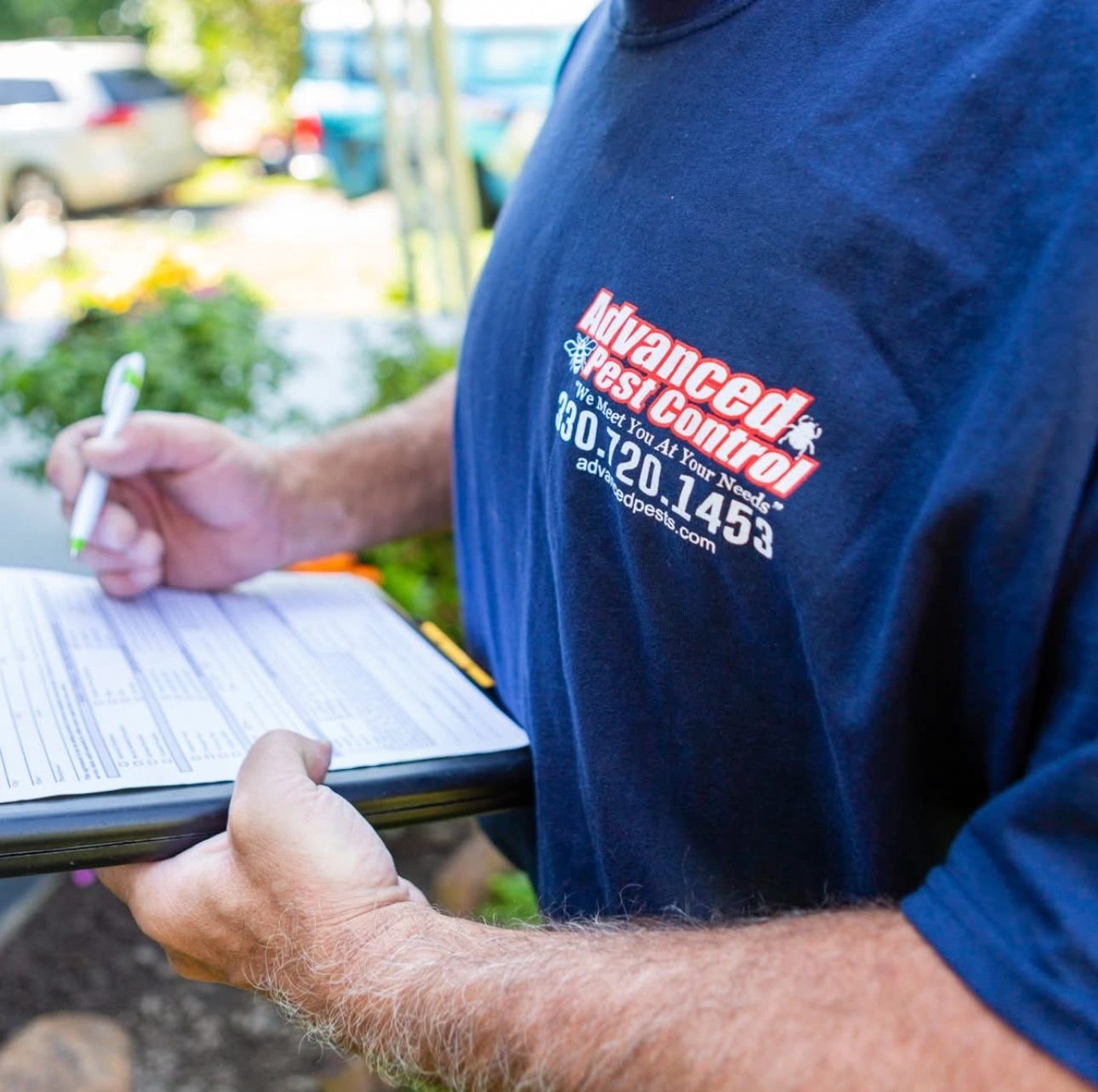 Person wearing an Advanced Pest Control shirt holding a clipboard and pen.