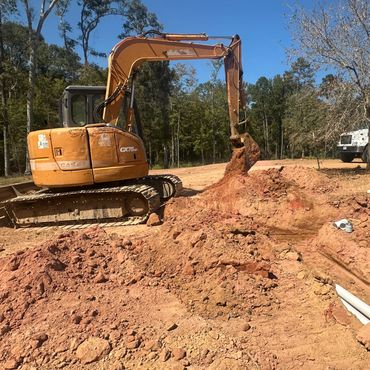 Yellow excavator digging soil in a clearing.