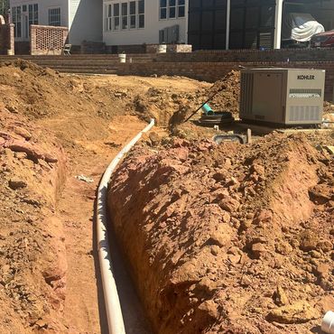 Trench with a pipe and Kohler generator outside a house.