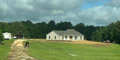 Newly built house on a large grassy hill under a cloudy sky.