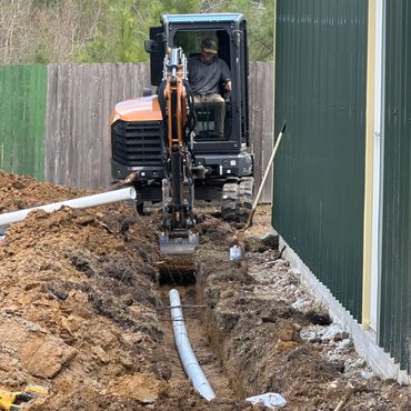 Excavator laying a pipe next to a green building.