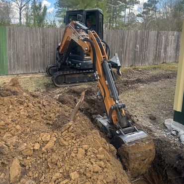 Mini excavator digging in a yard near a fence.