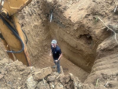 Man standing inside a deep excavation pit beside construction equipment.