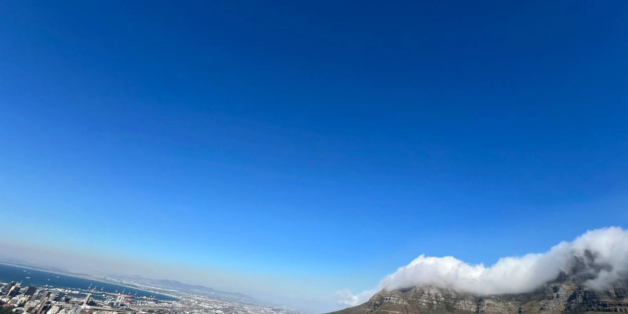 Cityscape with mountain covered in clouds under a clear blue sky.