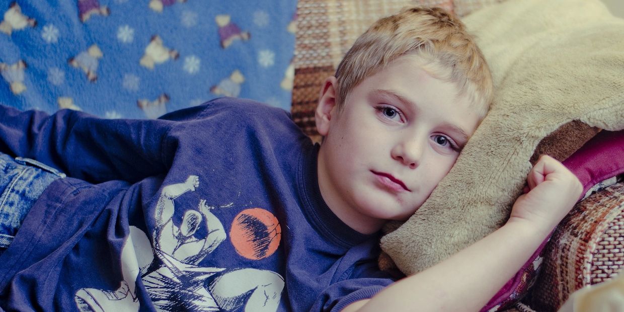 A boy with a blue long-sleeve shirt and jeans is laying on the couch with his head on a pillow.